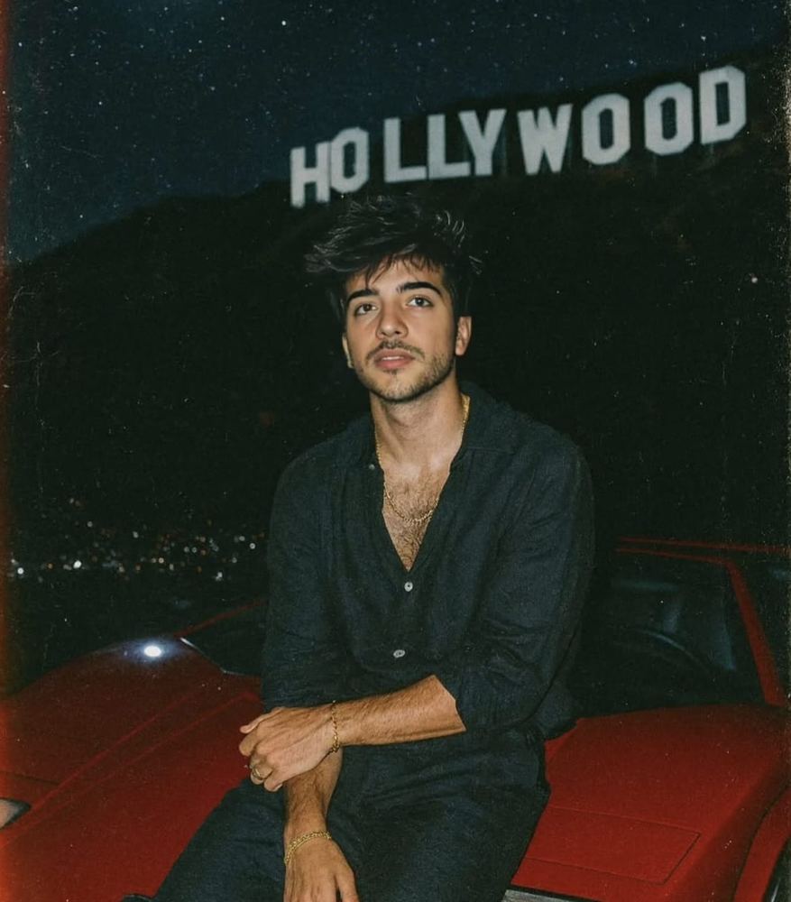 Nameloss de noche, sentado sobre un coche rojo con el cartel de Hollywood al fondo
